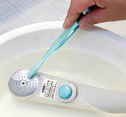 お酢を加えたお湯にシャワーヘッドを浸け、歯ブラシで磨いている写真